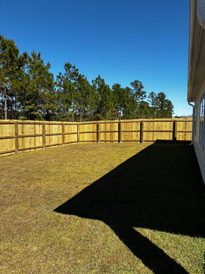 Wood privacy fence around a backyard with pine trees behind it