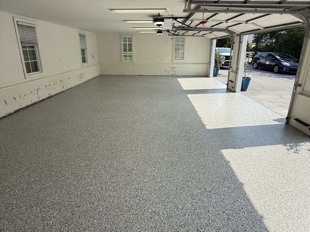 Garage floor with a gray full-flake epoxy coating, sunlight coming through the open garage doors