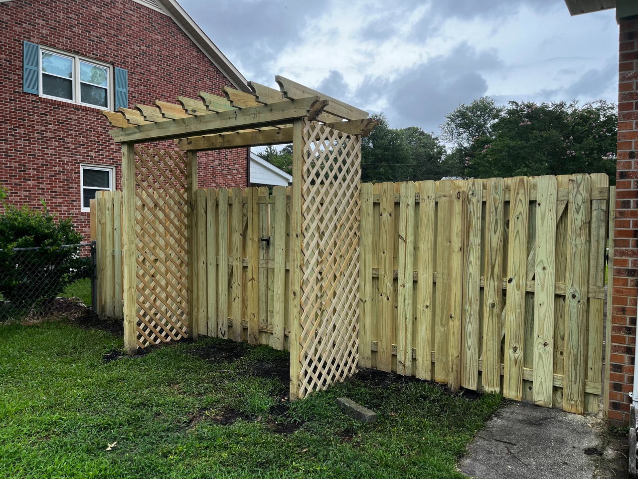 Wooden pergola with lattice side panels built over a fence gate